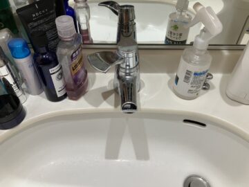 施工前の洗面台。レバーが横方向に倒れる旧型のシングルレバー水栓が設置されている。"