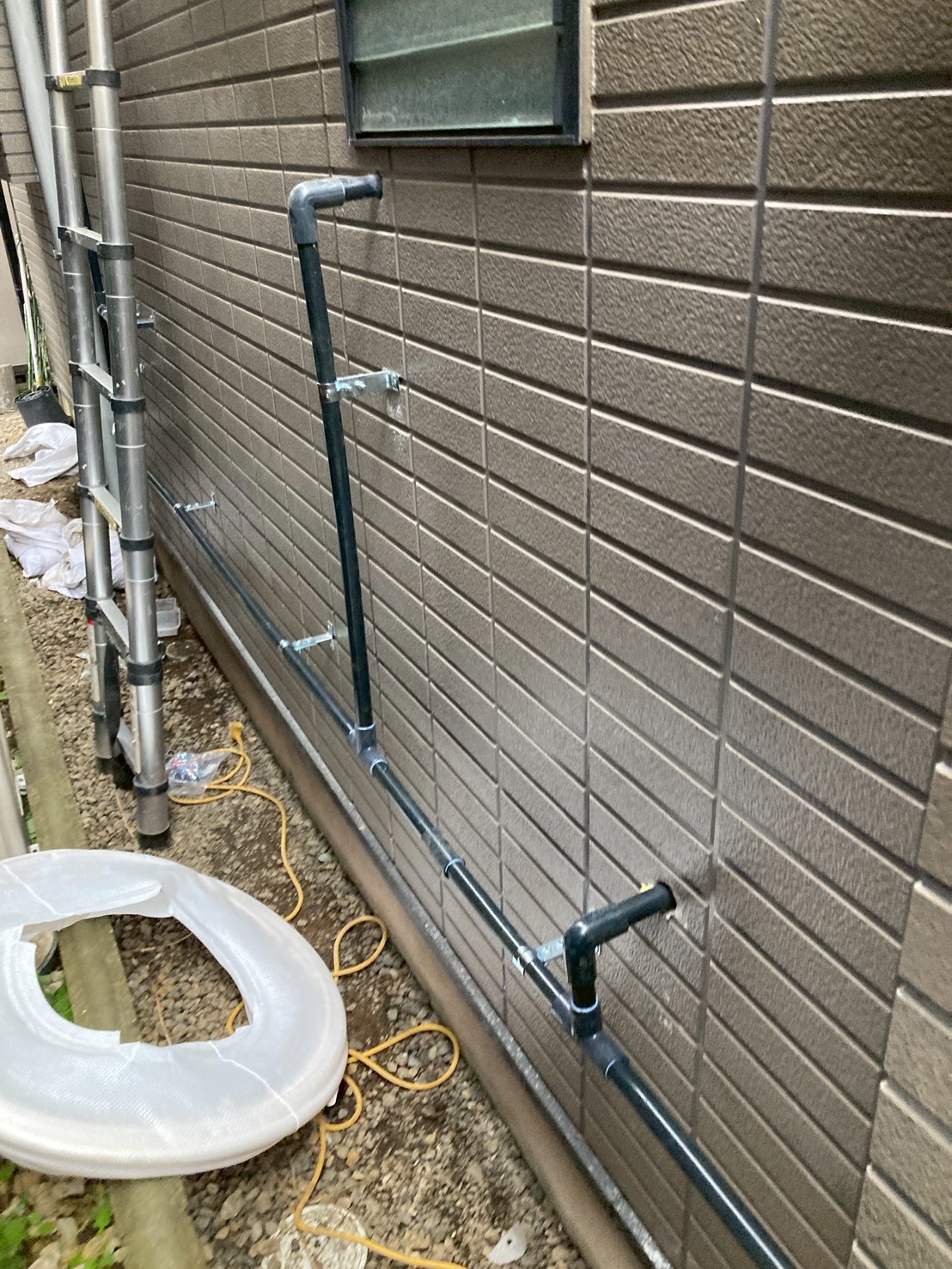 裏面外壁に沿って黒色の内管をブラケット固定しながら配管を延伸している様子