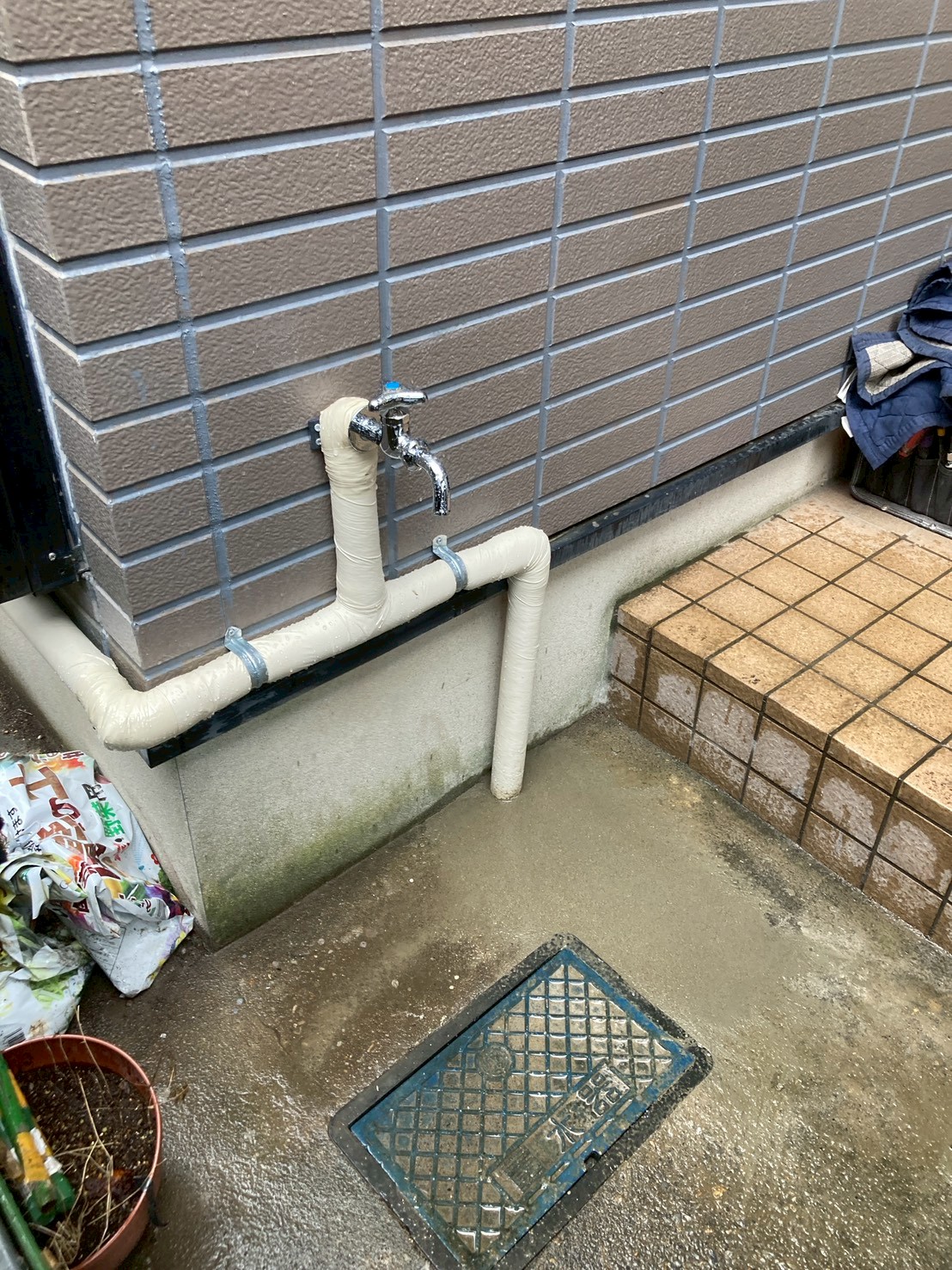 勝手口に新設した蛇口（単水栓）と新規配管。手前には止水栓の蓋が確認できる