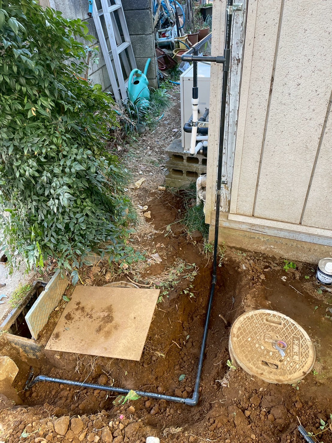 掘削した溝に新規HIVP給水管を配置し水道メーター周辺の接続を取り直している様子。遠方に給湯器まわりの配管も見える