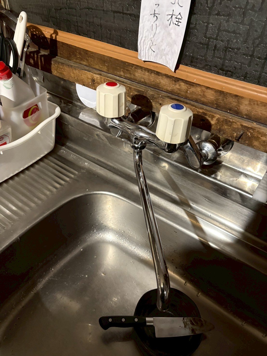 キッチンの既存2ハンドル混合水栓。「水栓とりくく」というメモが貼られた交換前の状態