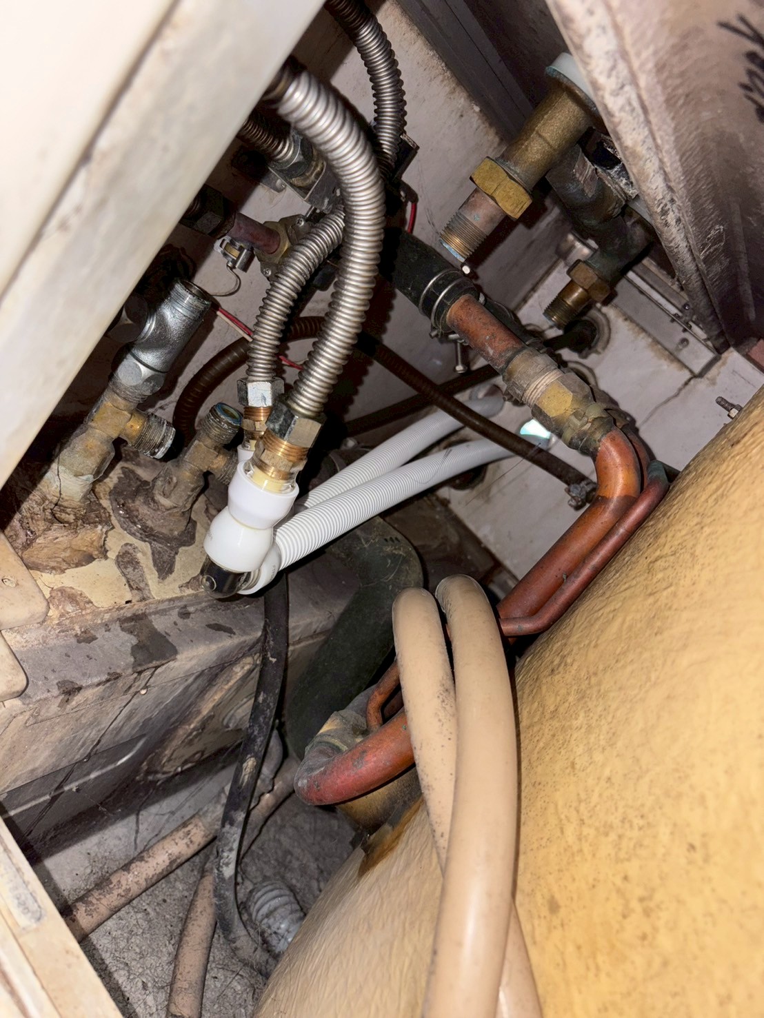 床下点検口内の既存配管。銅管とフレキ管が複雑に入り組み、錆・緑青が広がっている