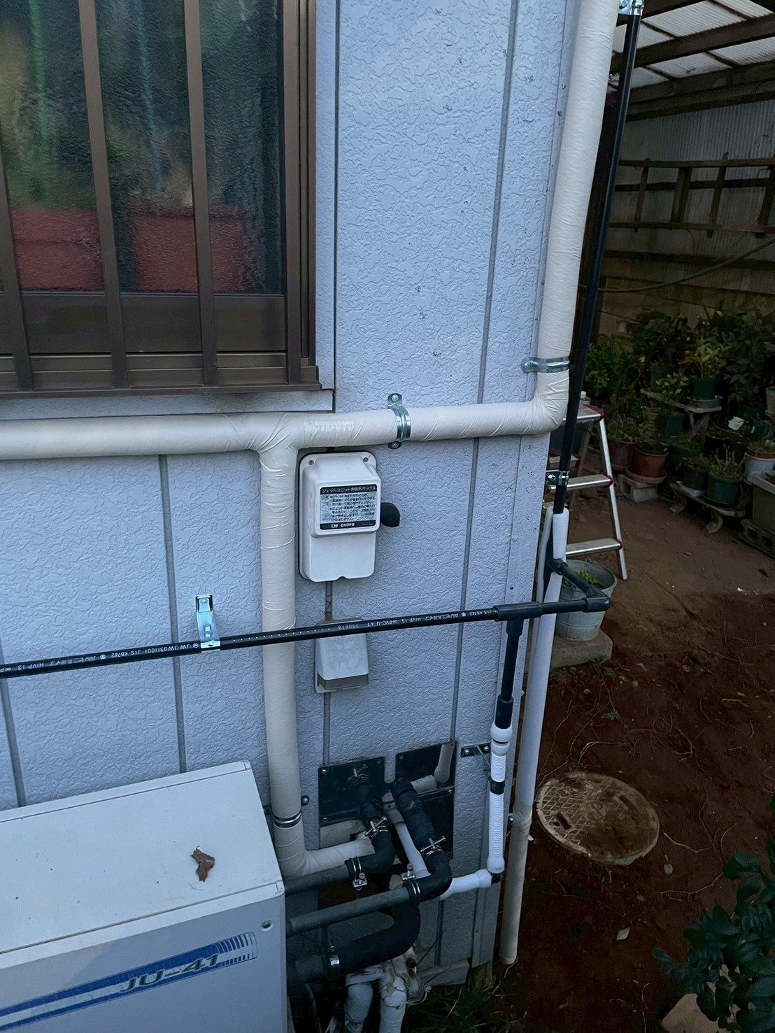 外壁面に保温付き給湯管（白）と給水管（黒HIVP）の2系統が並走して敷設完了。外部止水栓ボックスも設置