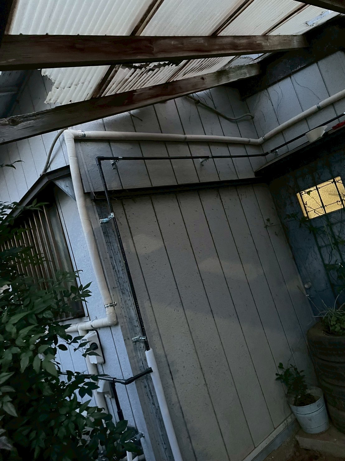 建物裏面と側面コーナー部の外壁に新規配管（白保温管・黒HIVP管）を這わせた全体像（夜間撮影）