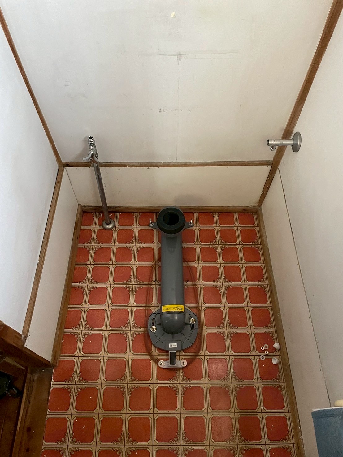 既存便器撤去後のトイレ床面。排水フランジと新規給水のアングル止水栓・温水洗浄便座用給水口が設置されている