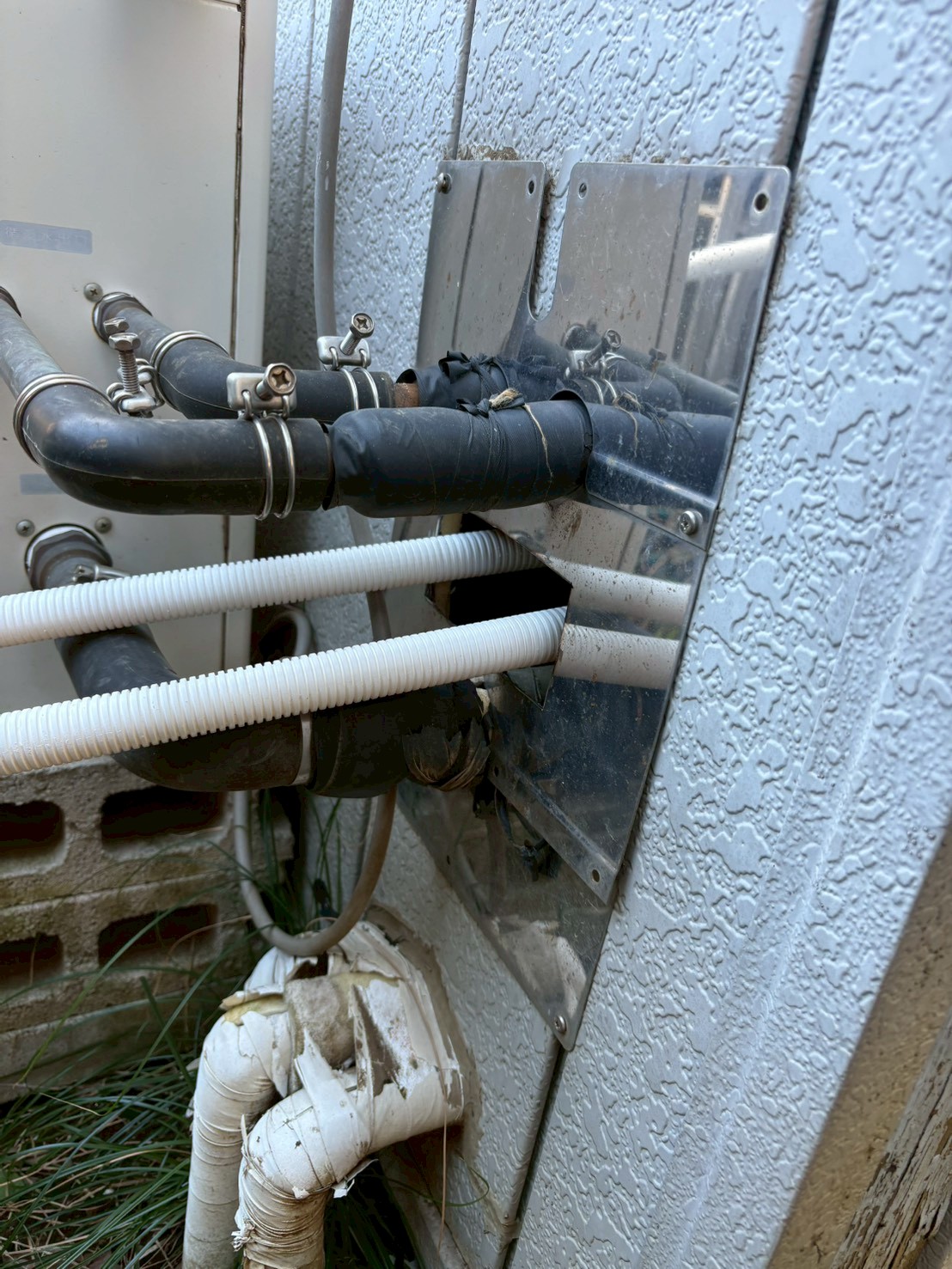 建物への既存配管貫通部。ビニルテープで応急処置された老朽配管が複数束になって壁を貫通している