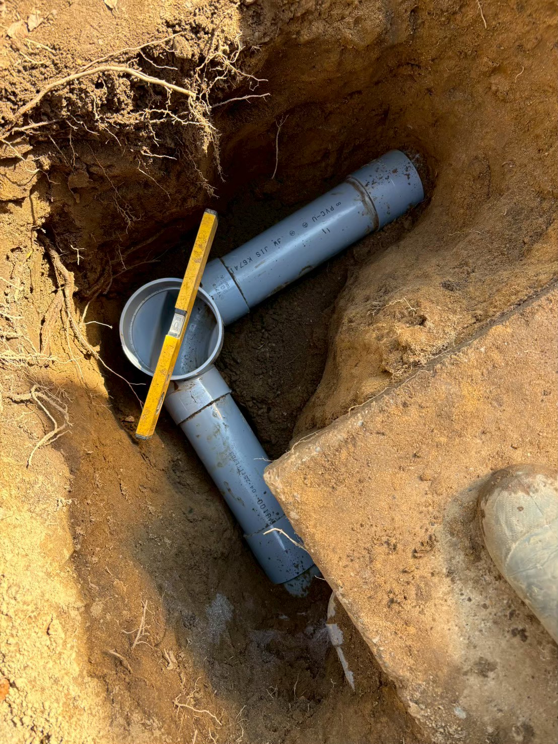 新しい塩ビ排水管（VU管）が地中に設置された状態。水平器で勾配を確認しながら配管工事中