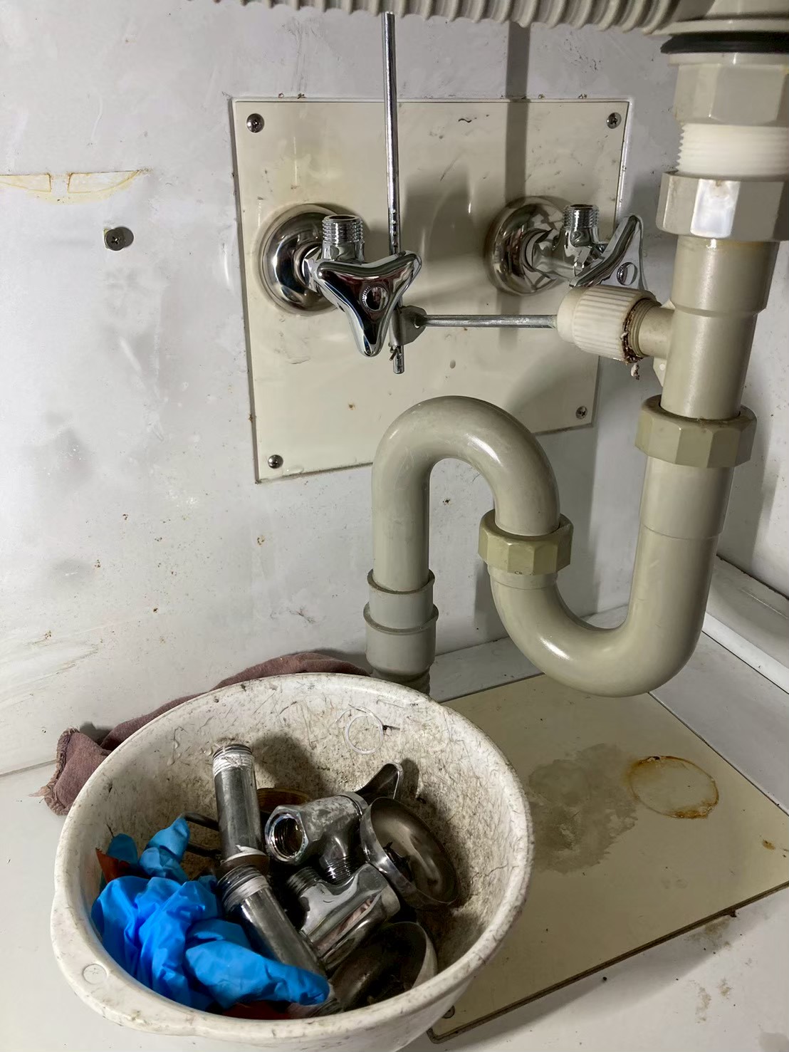 キャビネット内に新しい止水栓2本を取り付けた状態。取り外した旧部品がボウルにまとめられている