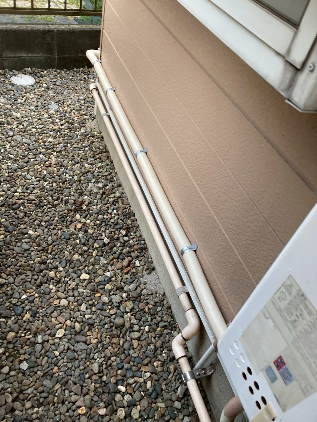 外壁基礎沿いに2本の新規保温配管をブラケット固定しながら延伸した様子