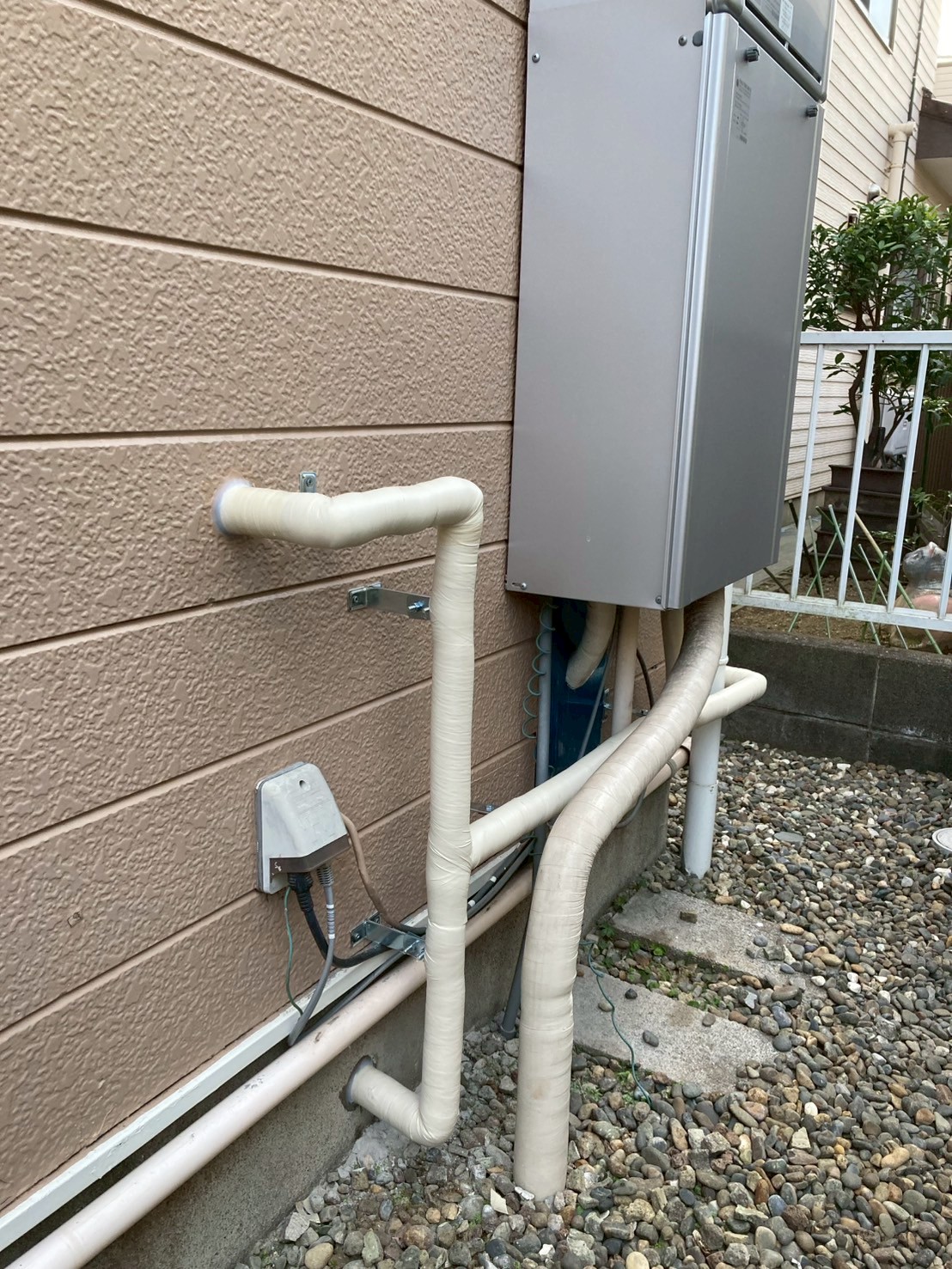 交換後の新しい給湯器と壁面に固定された新規保温配管の全景。左上に洗濯機用給水口も設置