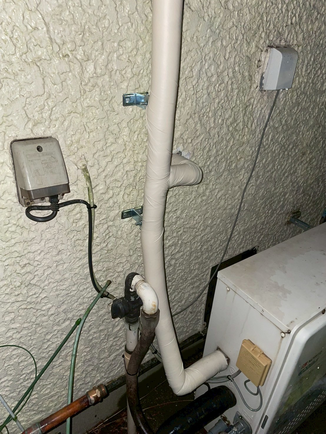 給湯器付近の外壁。古い銅管の接続跡と新規配管の分岐継手が確認できる