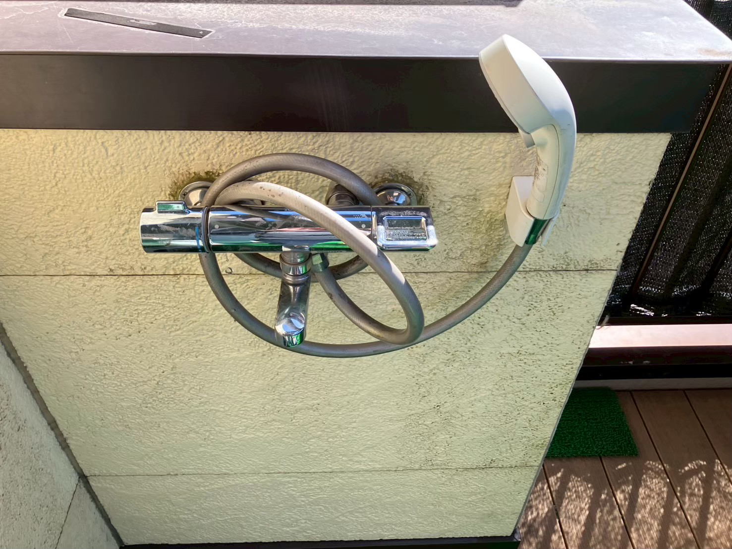 テラスに設置された既存のサーモスタット混合水栓。水垢・黒ずみが付着し周囲の外壁に苔汚れが広がっている