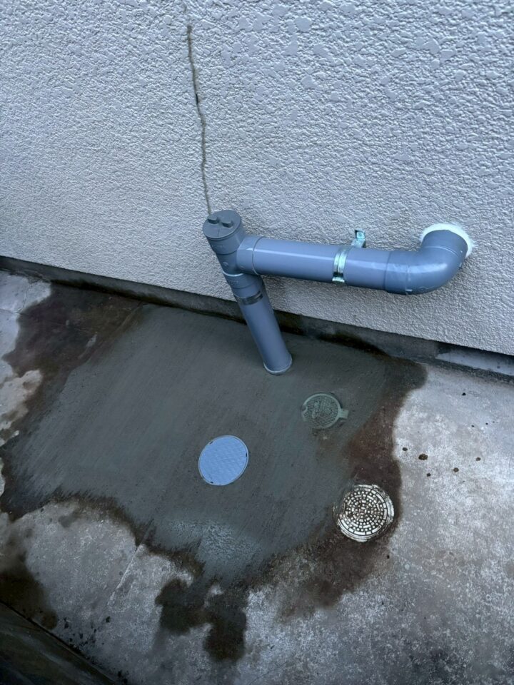 屋外アフター。新しい塩ビ管がL字継手で外壁に接続。新しい桝蓋が地表に設置されている