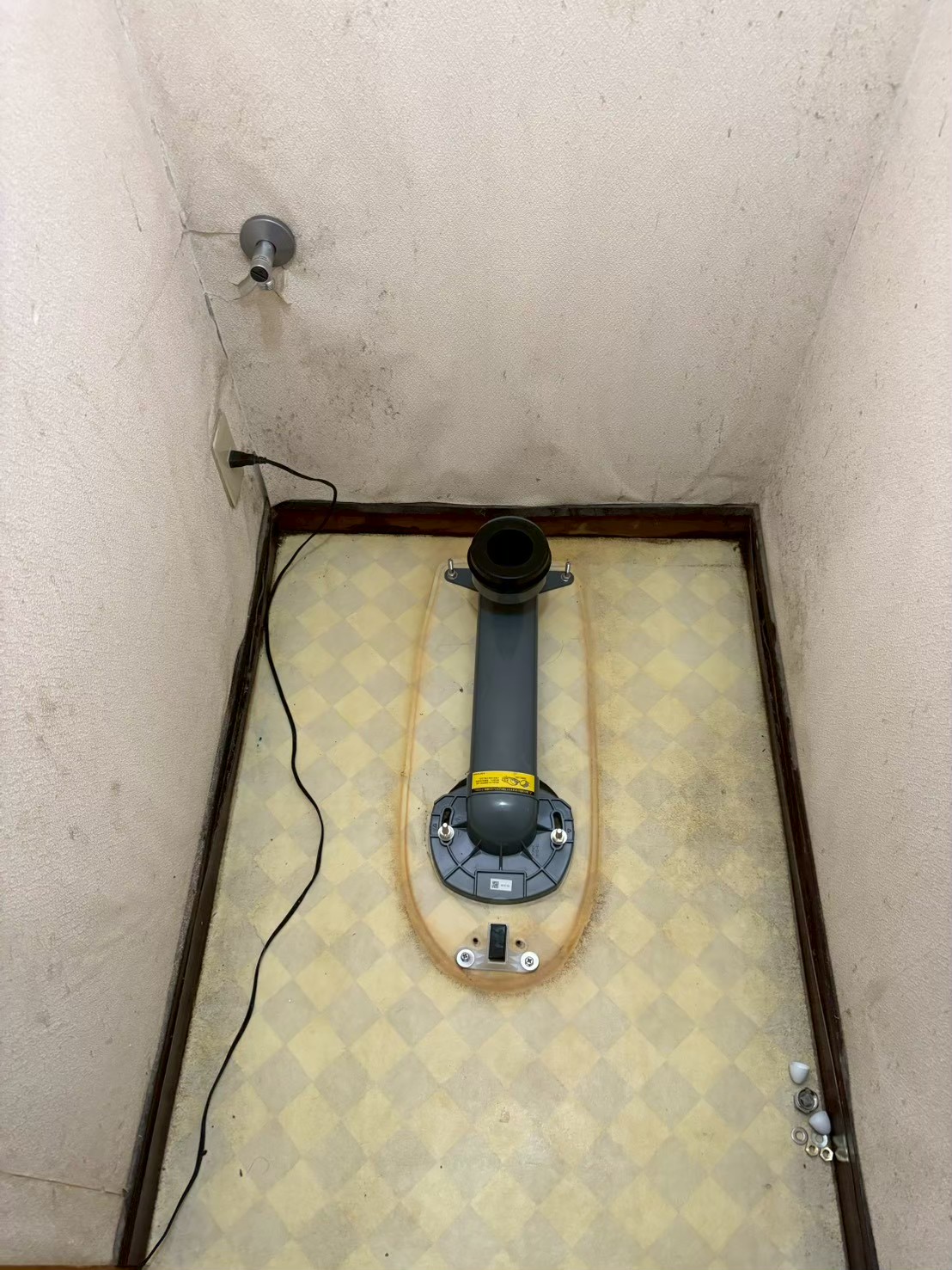 旧便器撤去後の床面。排水フランジが露出し、床全体に黄色い尿石・水漏れの染みが広がっている