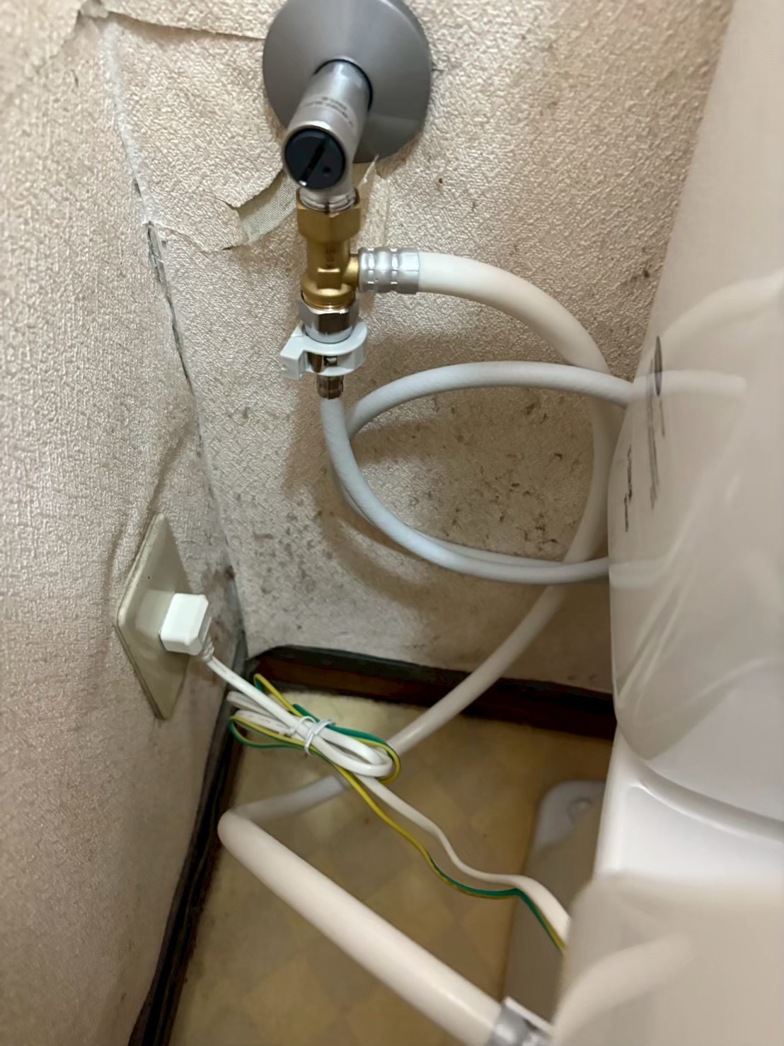新しいトイレ設置後の止水栓・給水ホース周辺。壁のクロスが剥がれており長期間の漏水による湿気の影響が確認できる