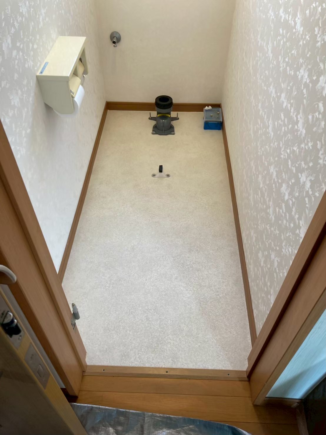 新しいクッションフロアの施工が完了した状態。白系の清潔感ある床材が張り替えられ、排水フランジと止水栓のみが設置されている便器設置前の状態