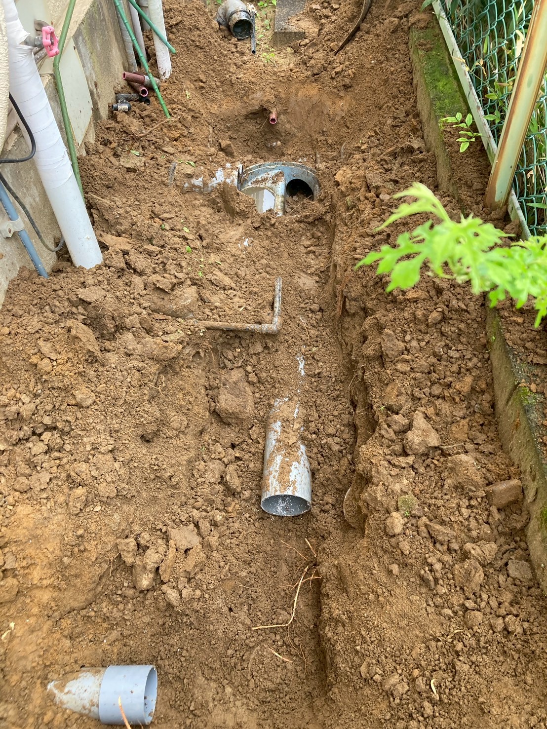 建物外壁沿いに掘削した溝。老朽化した鋳鉄製排水管が地中に埋まっており錆・腐食が確認できる