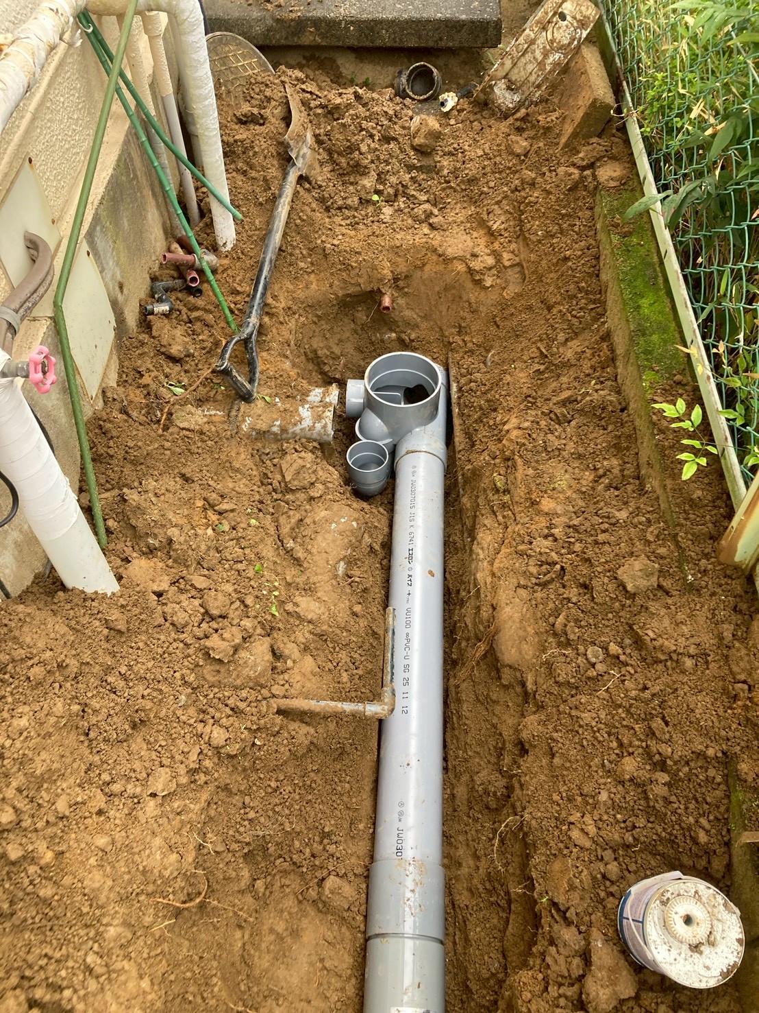 建物外壁沿いの掘削溝を上から見た状態。新しい塩ビ排水管が敷設中で合流継手が確認できる