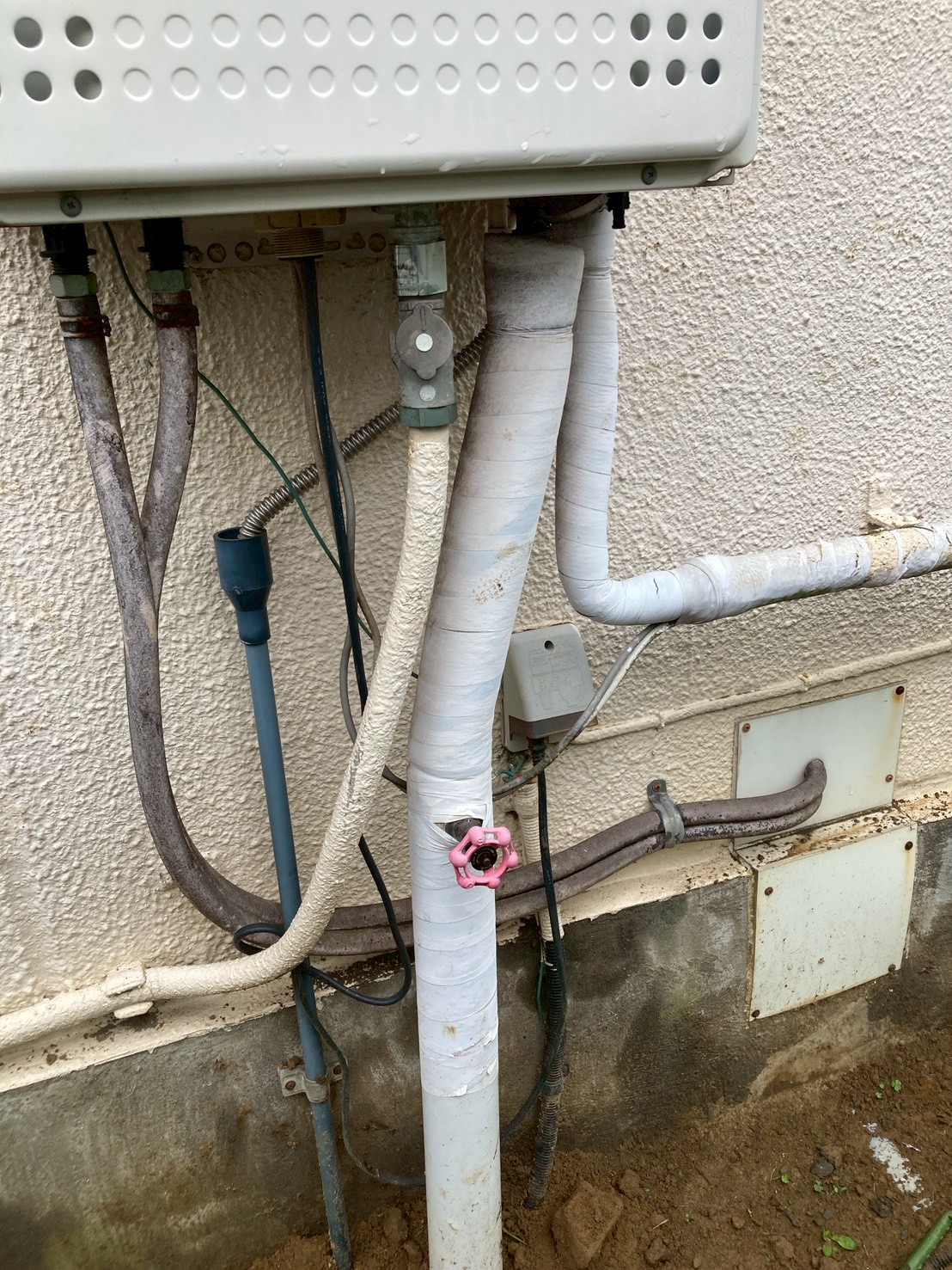 建物外壁と既存の配管まわり。保温材の劣化した配管と給湯器が確認できる