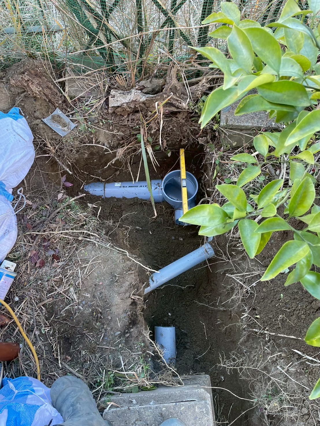 掘削したトレンチに新規VP管が2系統配置されている。スケールで寸法を確認しながら接続・勾配調整を実施している作業中の様子