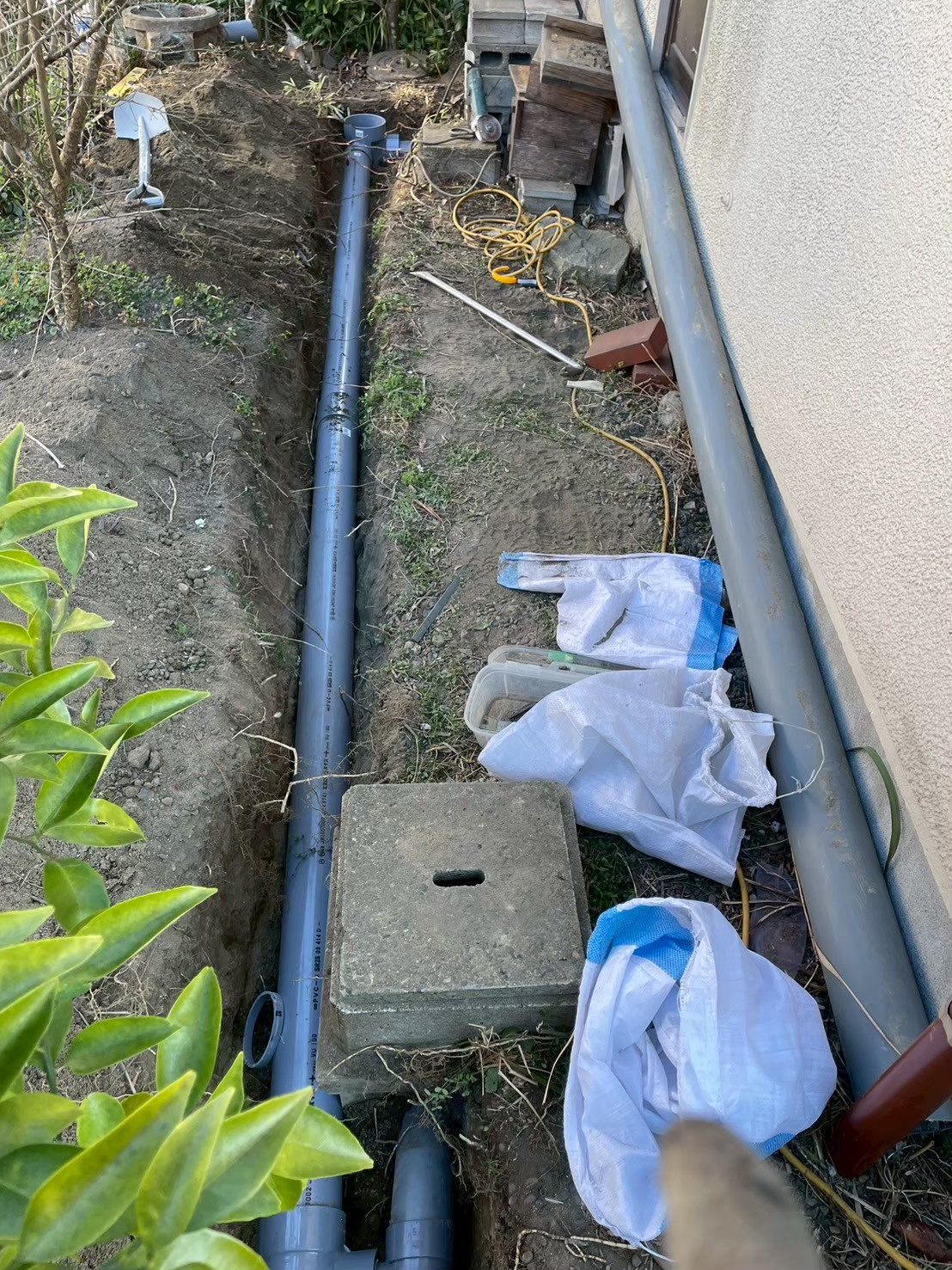 建物外壁沿いに新設VP管が全長にわたって配置された状態。複数の排水桝も整備され、埋め戻し前の全体確認中