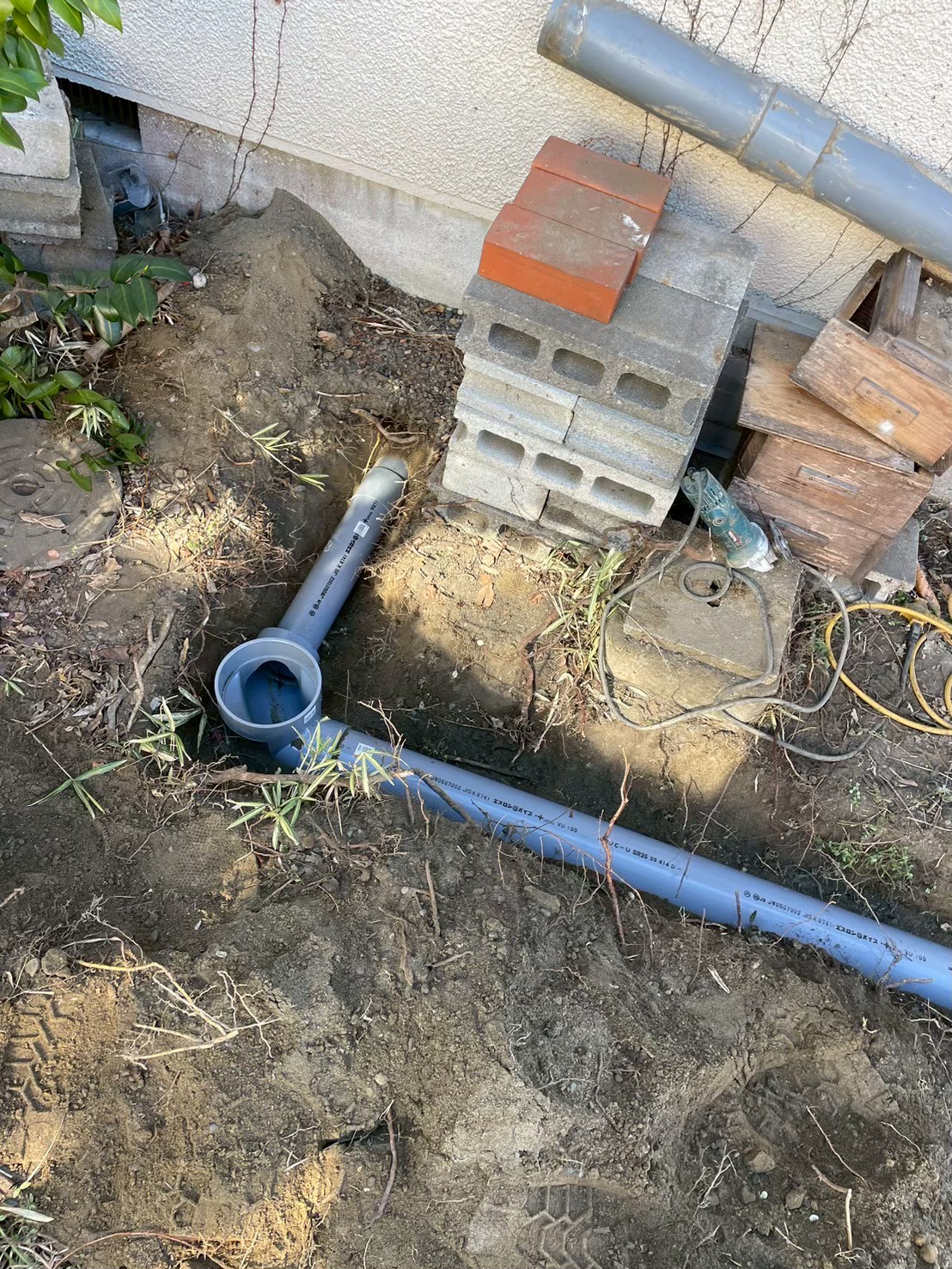 建物基礎外壁の排水管貫通部。建物内部からのVP管がエルボで方向転換して屋外横引き管に接続されている施工中の状態