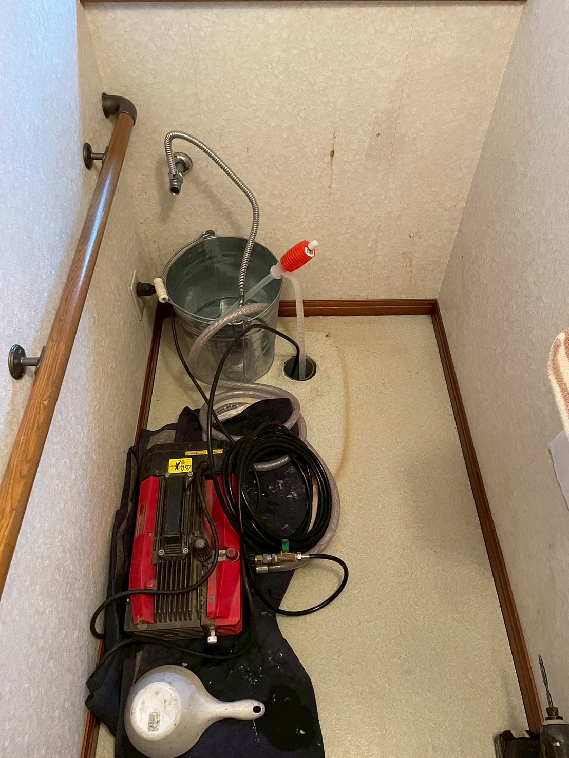 便器を撤去したトイレ室。Asada製高圧洗浄機・洗浄ホース・水受けバケツが設置されている。床には作業前の水染みの輪染みが残る