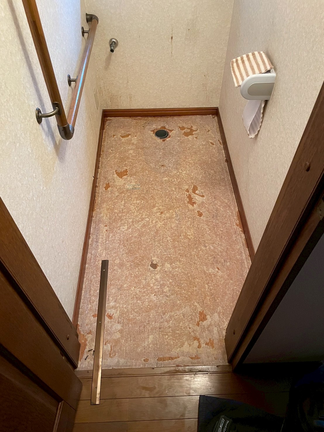 既存クッションフロアを全面撤去した後の床面。床材の裏側のメッシュと接着剤跡が残っており、劣化の状況が確認できる。中央に排水フランジが露出している