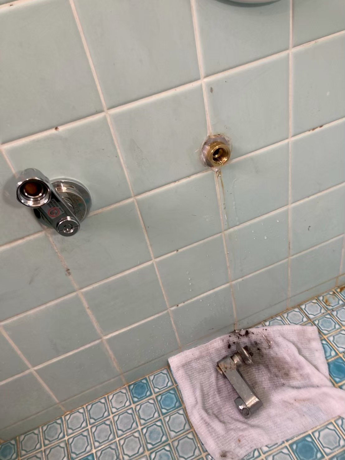 浴室壁の配管口アップ。右側の給湯側配管のネジ部が折れており、水がしたたり落ちている