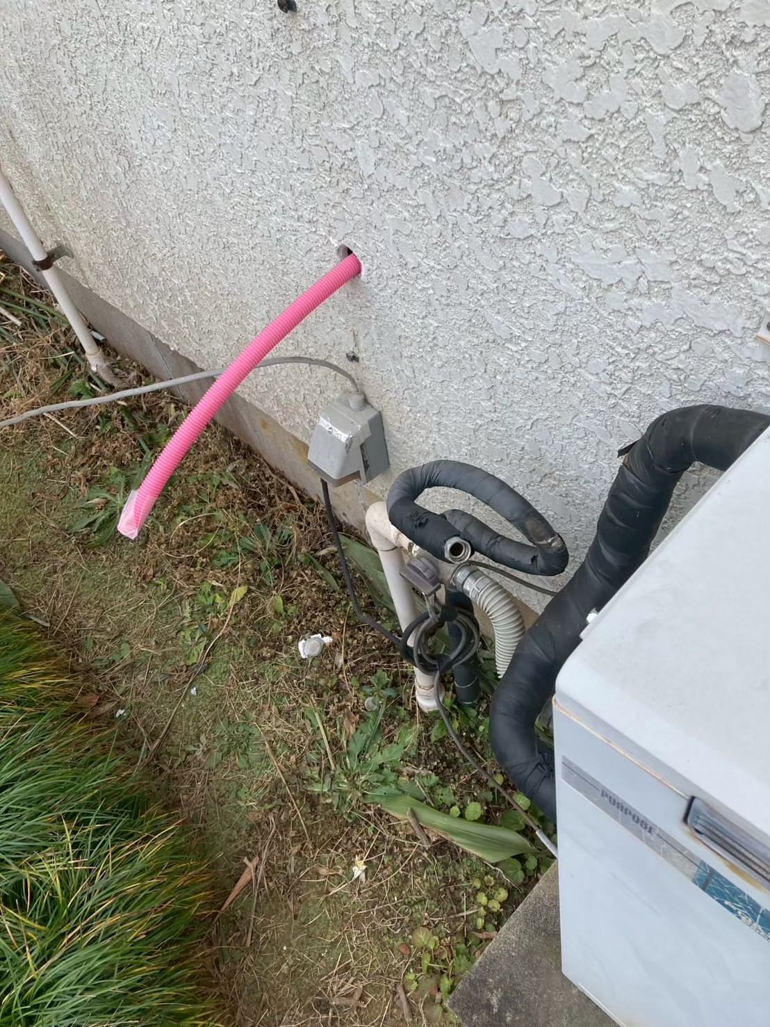 外壁下部からピンク色のさや管（断熱被覆給水管）が引き出されてきた状態