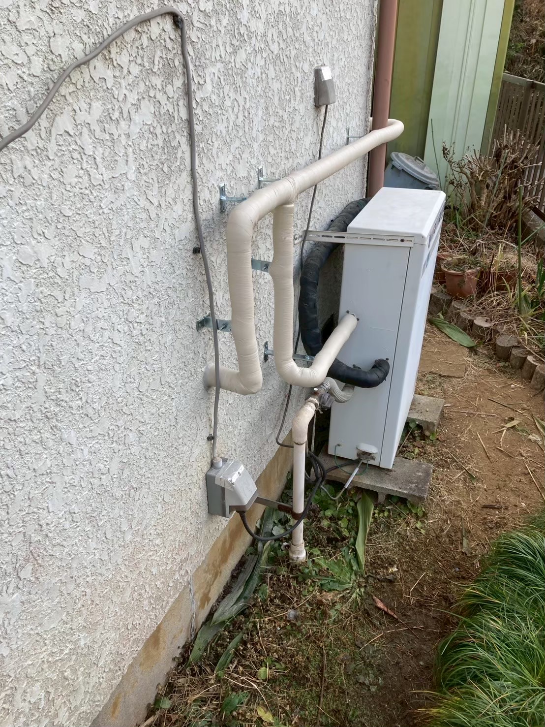 断熱材で被覆された完成後の屋外給水管。外壁にブラケットで固定されている