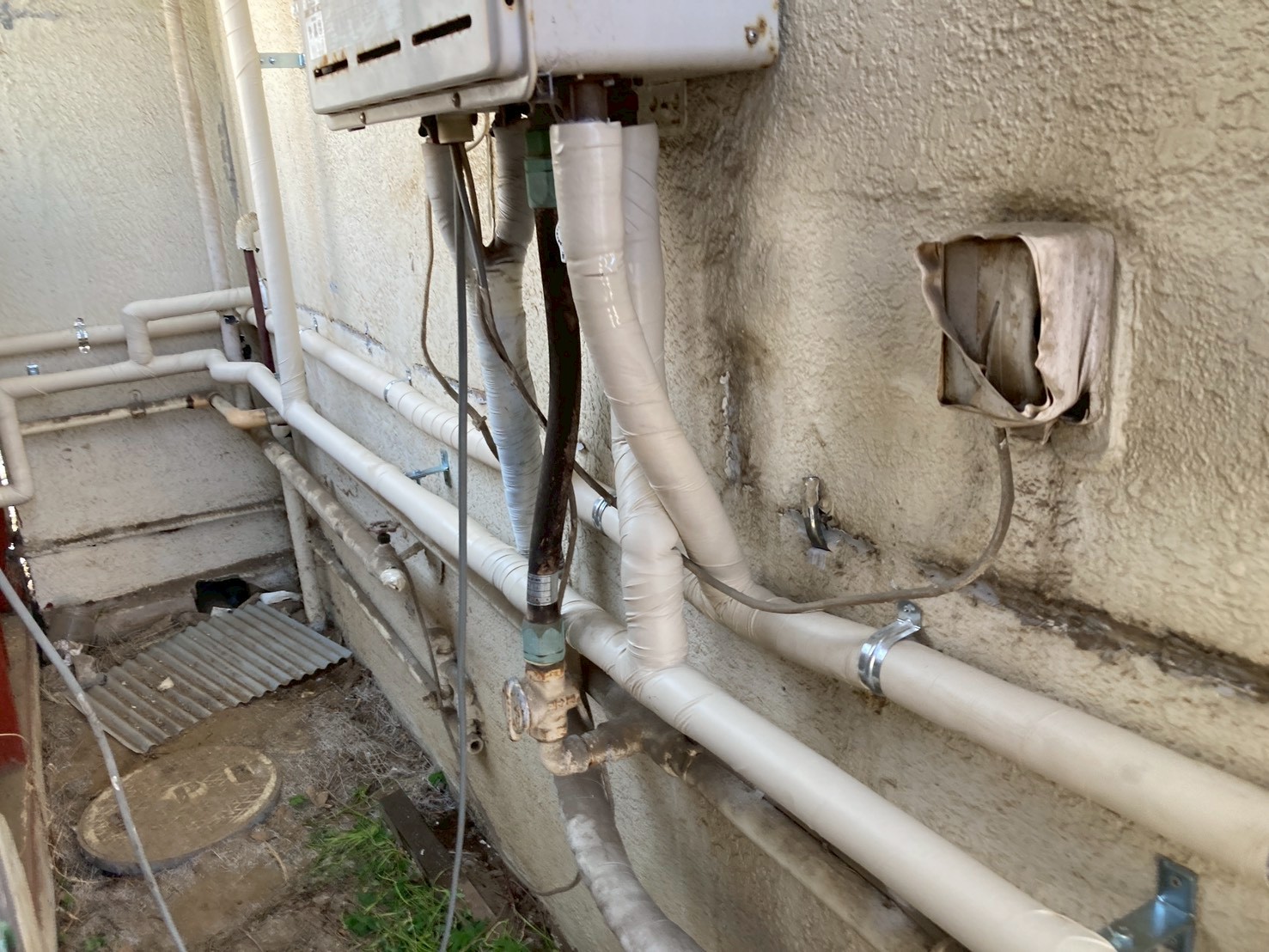 施工前の外壁配管まわり。古い配管の保温材が劣化・ボロボロになり中の配管が露出している