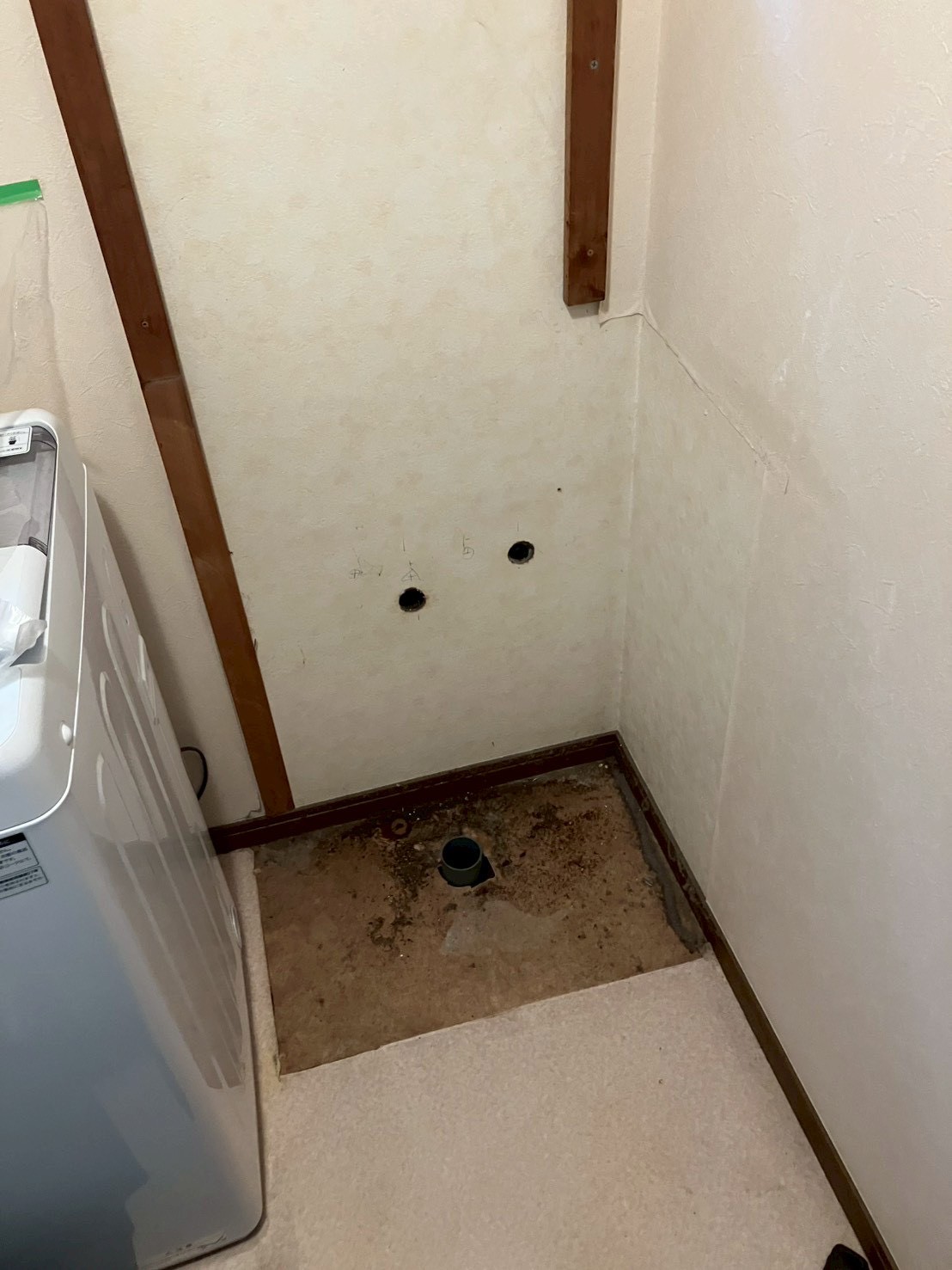 洗面台撤去後の壁。新規の給水・給湯取り出し穴が開けられ床にも配管引き出し穴がある状態