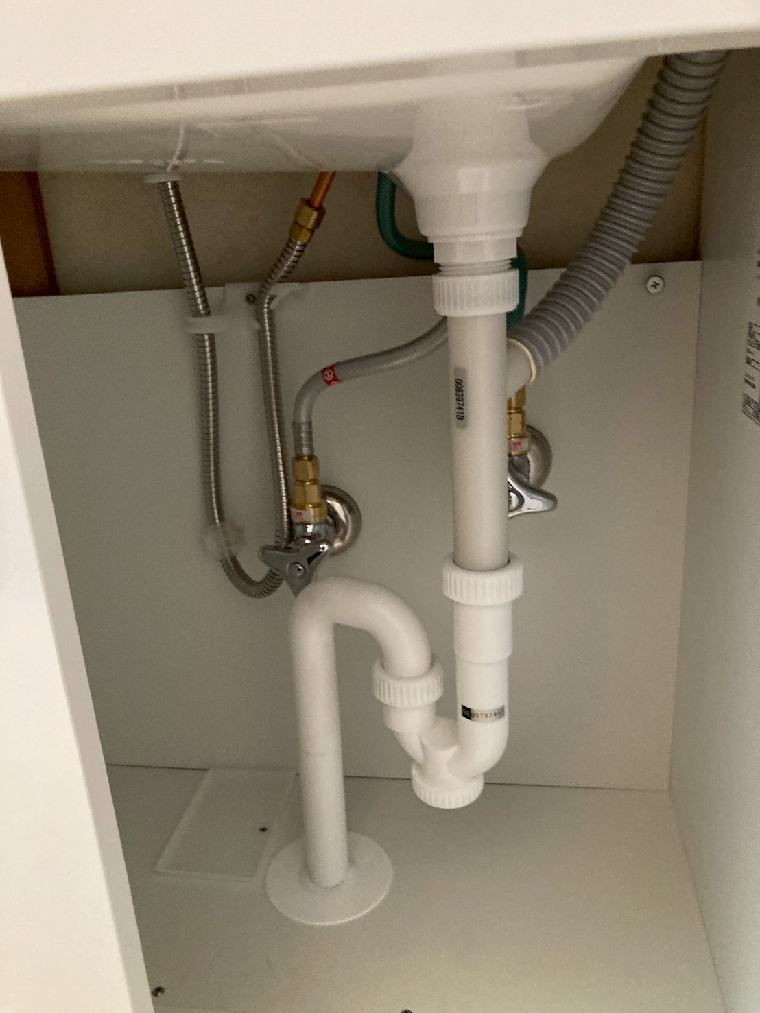 洗面化粧台キャビネット内部の完成後配管。湯・水フレキ管と新品排水トラップが整備されている