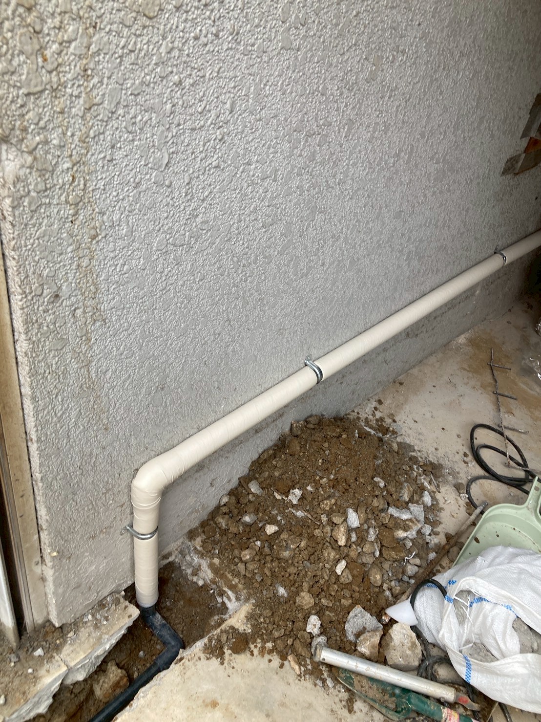 外壁基礎付近で新規配管を地中から立ち上げて固定している工事中の様子