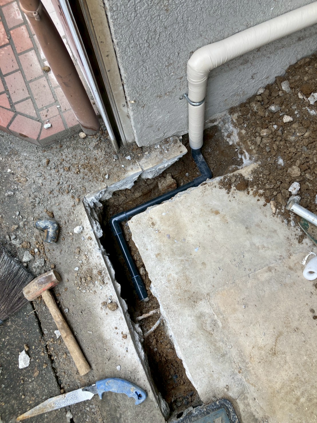 ガレージ入口付近のコンクリート床を斫った箇所に新規配管を引き込んでいる工事中の様子